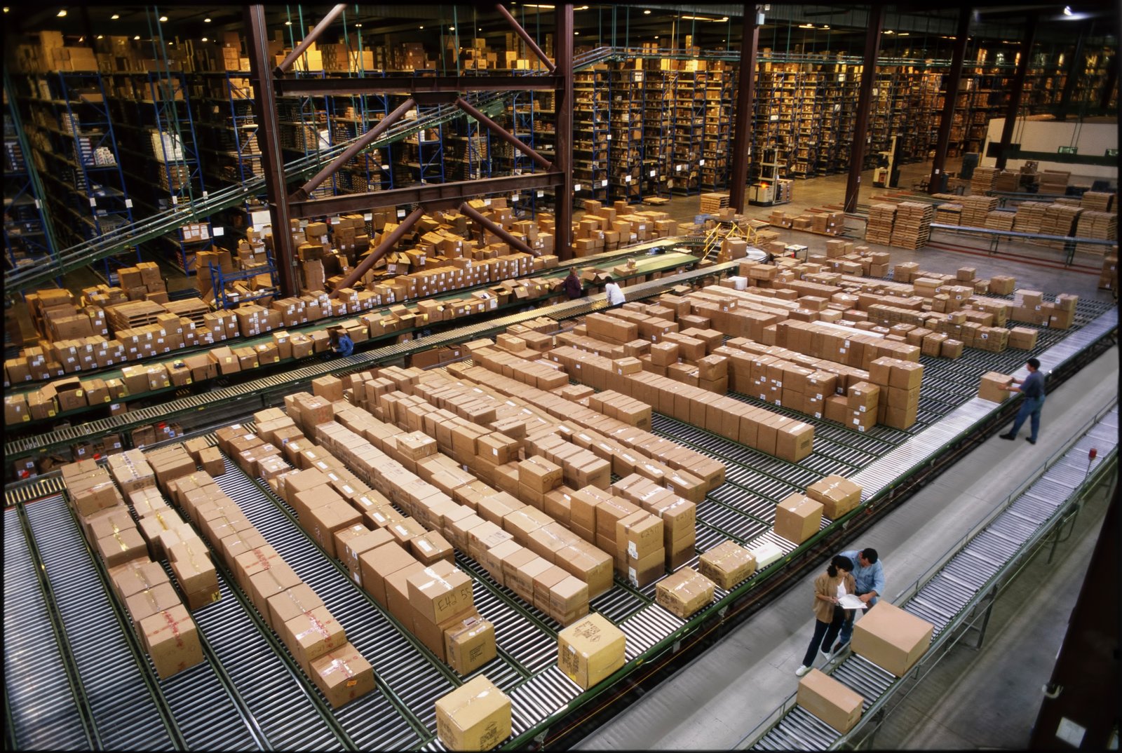 Overview of a large industrial distribution warehouse storing products in cardboard boxes on conveyor belts and racks.